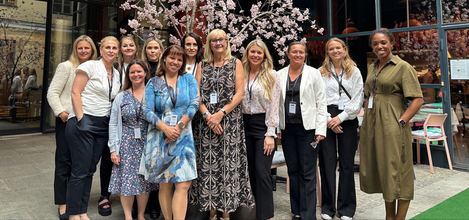 A group of business women pose in a group in front of a shrub in blossom